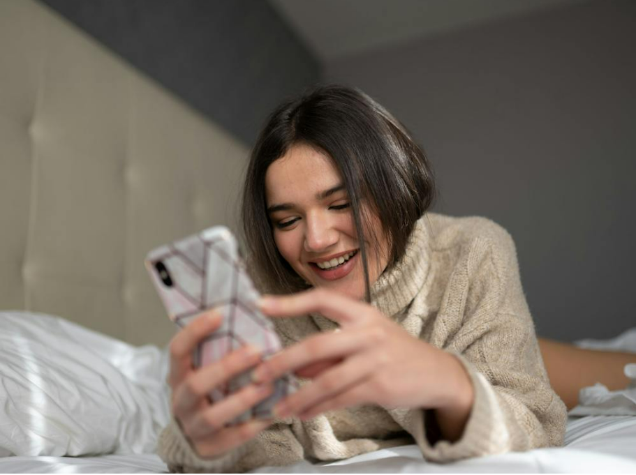 cheerful-women-texting-on-phone-smiling-in-bed
