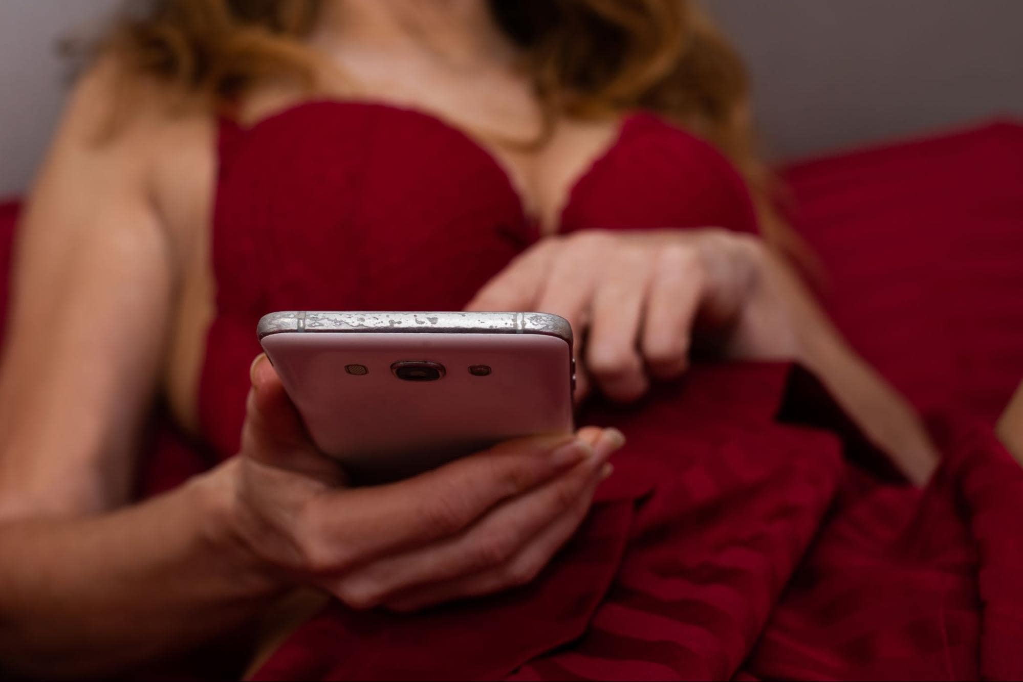 woman-in-red-lingerie-using-adult-dating-apps-on-phone-in-bed